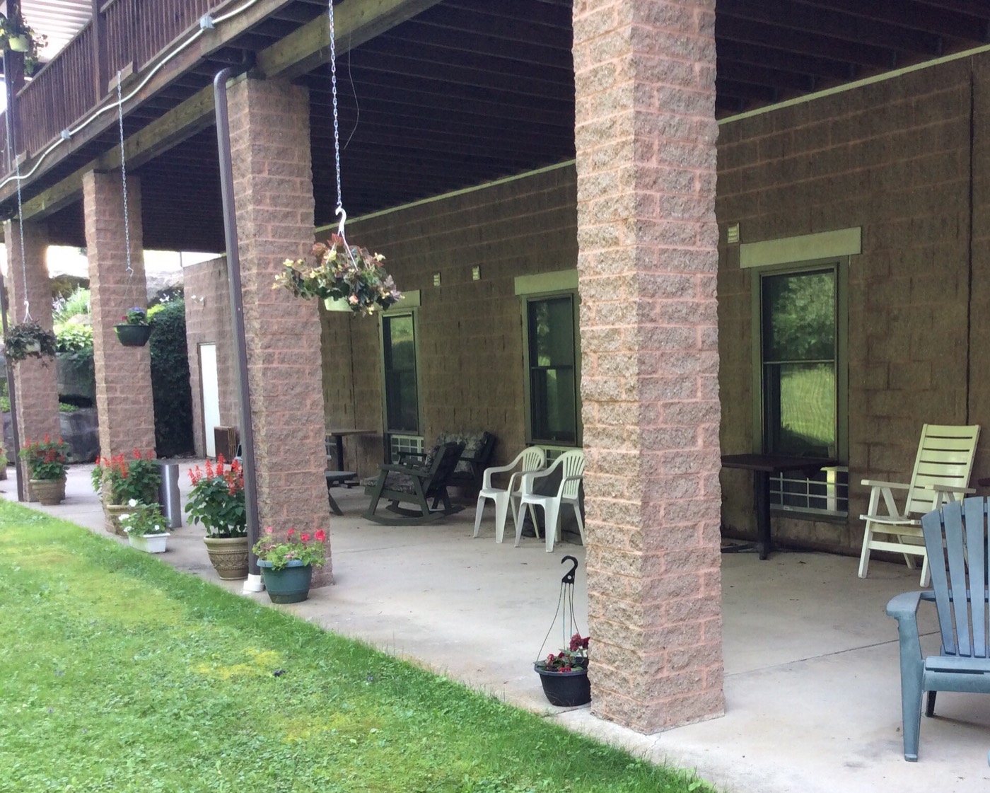 Covered brick patio with rocking chairs and hanging flower baskets overlooking the green lawn at Crystal Waters