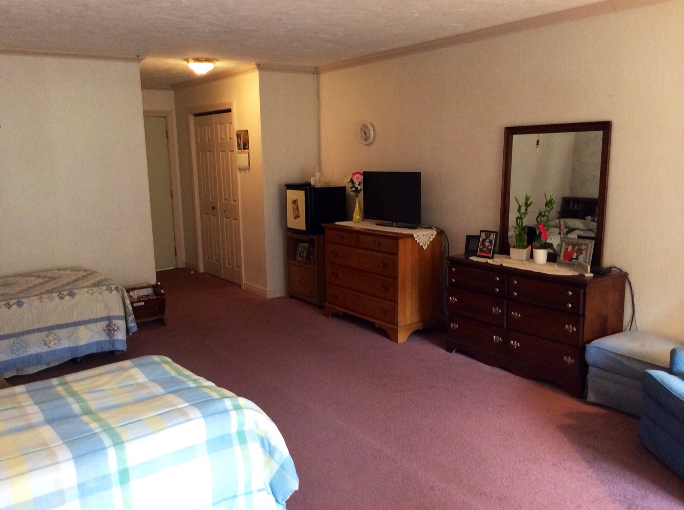 A large, fully furnished resident room with a bed, dresser, television, and comfortable seating